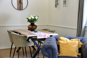 Un coin repas comprenant une table, des chaises, un vase avec des fleurs et un canapé avec un coussin.