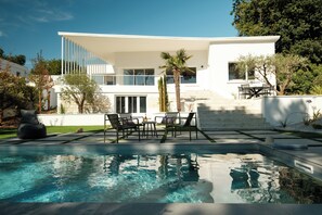 Una casa moderna con piscina, muebles de exterior y una escalera que lleva a un balcón.