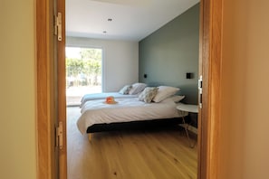 A bedroom with two beds, a wooden floor, and a view of a fenced outdoor area. - Villa les Pins - Royan, 350 meters from the beach (Royan)