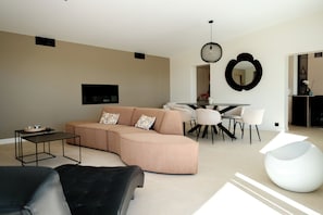A modern living room with a sectional sofa, a dining table with chairs, a black leather armchair, and a white pouf. - Villa les Pins - Royan, 350 meters from the beach (Royan)