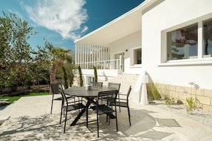 A modern outdoor patio with a round table and chairs, surrounded by a white building with large windows and a balcony. - Villa les Pins - Royan, 350 meters from the beach (Royan)