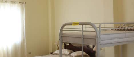 Quarto com beliches, ventilador de teto e janela com cortinas.