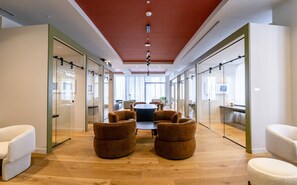 Un espacio de oficina moderno con una mesa de reuniones central, asientos cómodos, paredes de vidrio y piso de madera.