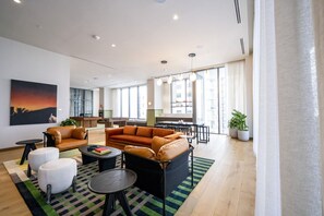 Un salon moderne avec un canapé, des fauteuils et une table basse. On aperçoit, au fond, un coin cuisine avec une table à manger et des chaises.