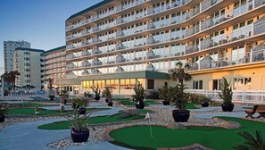 Un hotel de diversos pisos amb balcons, una zona de piscina amb gespa artificial i plantes en testos.