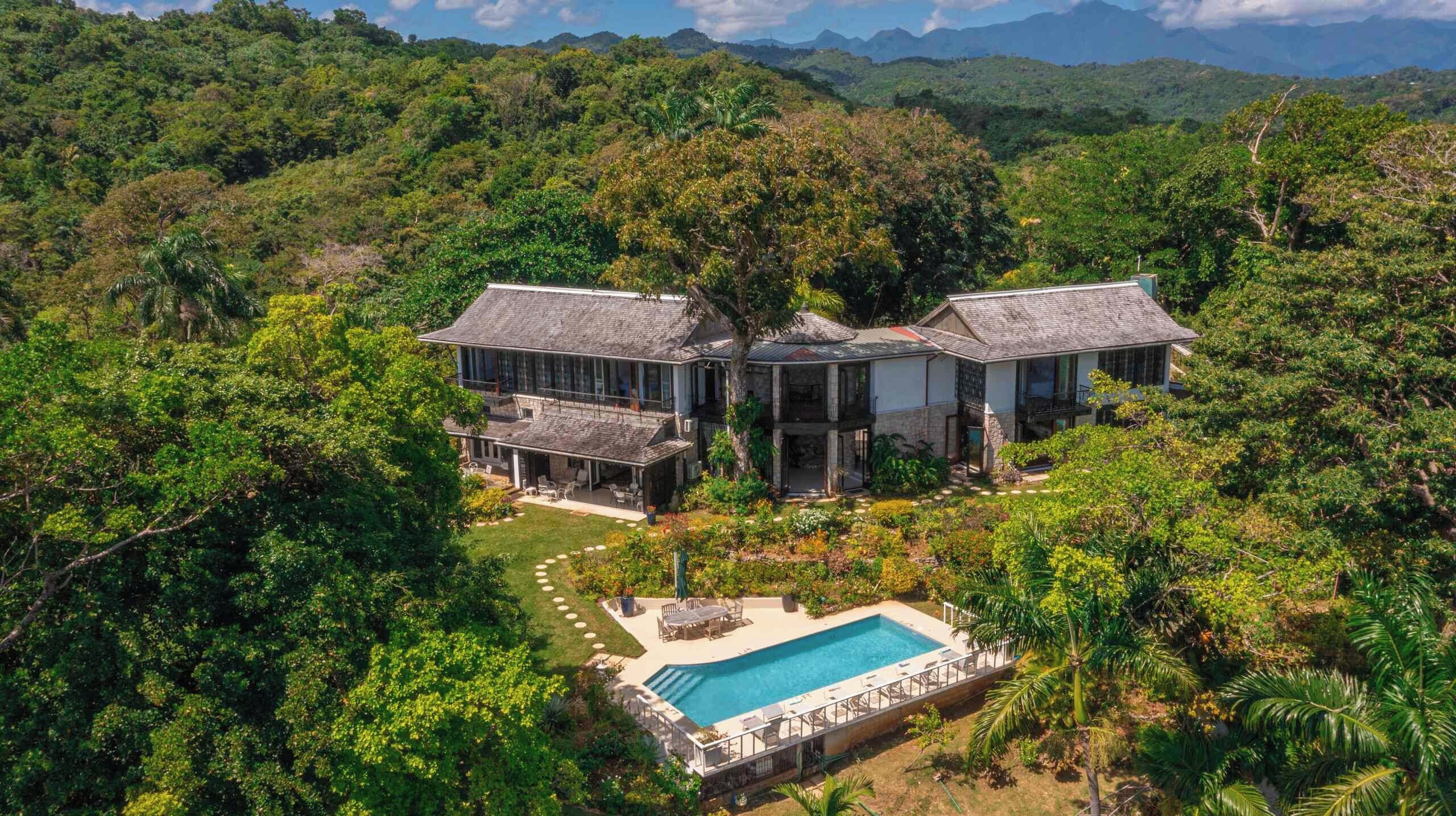 Une grande maison avec une piscine, entourée d’une végétation luxuriante.