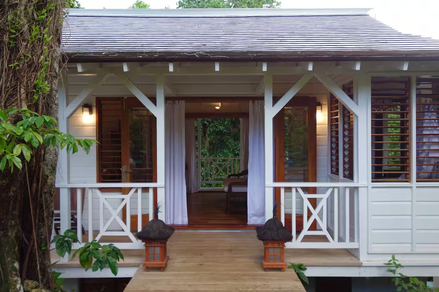 A white wooden house with a porch, a thatched roof, and a wooden deck.