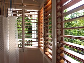 Un baño con ducha, una ventana con listones de madera y vistas al exterior.
