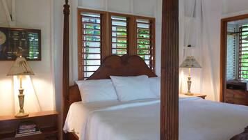 Een hemelbed met een houten hoofdeinde, wit beddengoed en twee bedlampen.