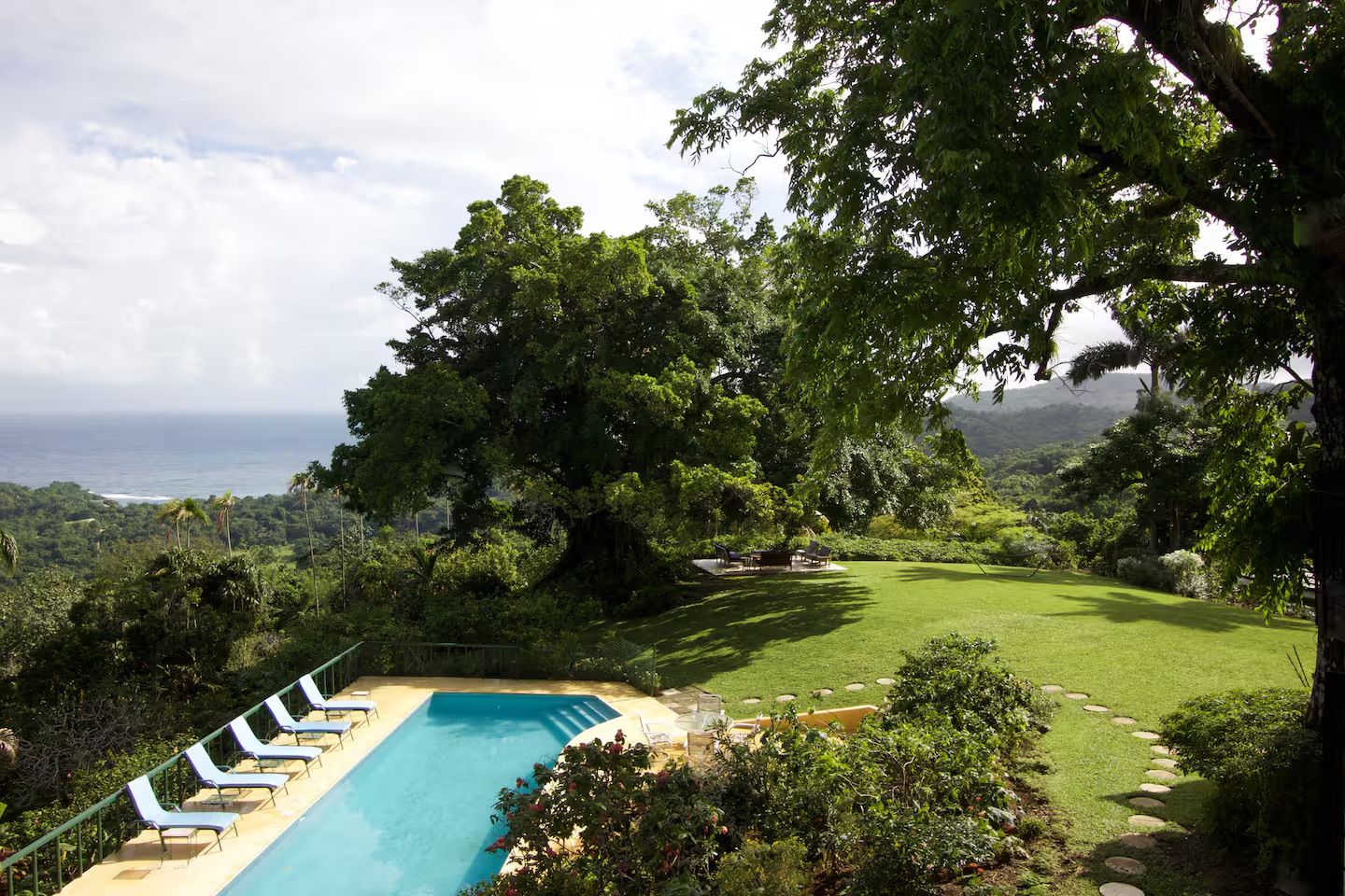 A pool with lounge chairs, a grassy area, and a view of the ocean.