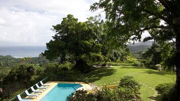 A pool with lounge chairs, a grassy area, and a view of the ocean.