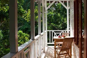 Eine hölzerne Veranda mit Tisch und Stuhl, umgeben von weißen Geländern und üppigem Grün.