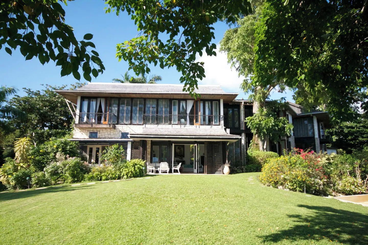 A two-story house with a covered patio, surrounded by lush greenery and a well-maintained lawn.