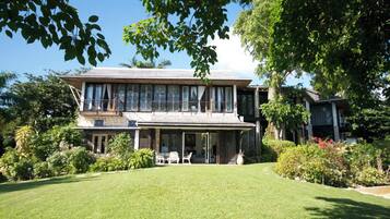 A two-story house with a covered patio, surrounded by lush greenery and a well-maintained lawn.