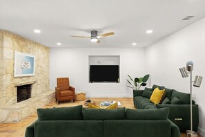 Ein modernes Wohnzimmer mit Kamin aus Stein, Deckenventilator, Flachbildfernseher und grünen Sofas.