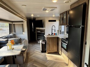A compact RV kitchen with a dining area, a sink, a stove, and a refrigerator. - Kiamichi Hideaway (Hodgen)