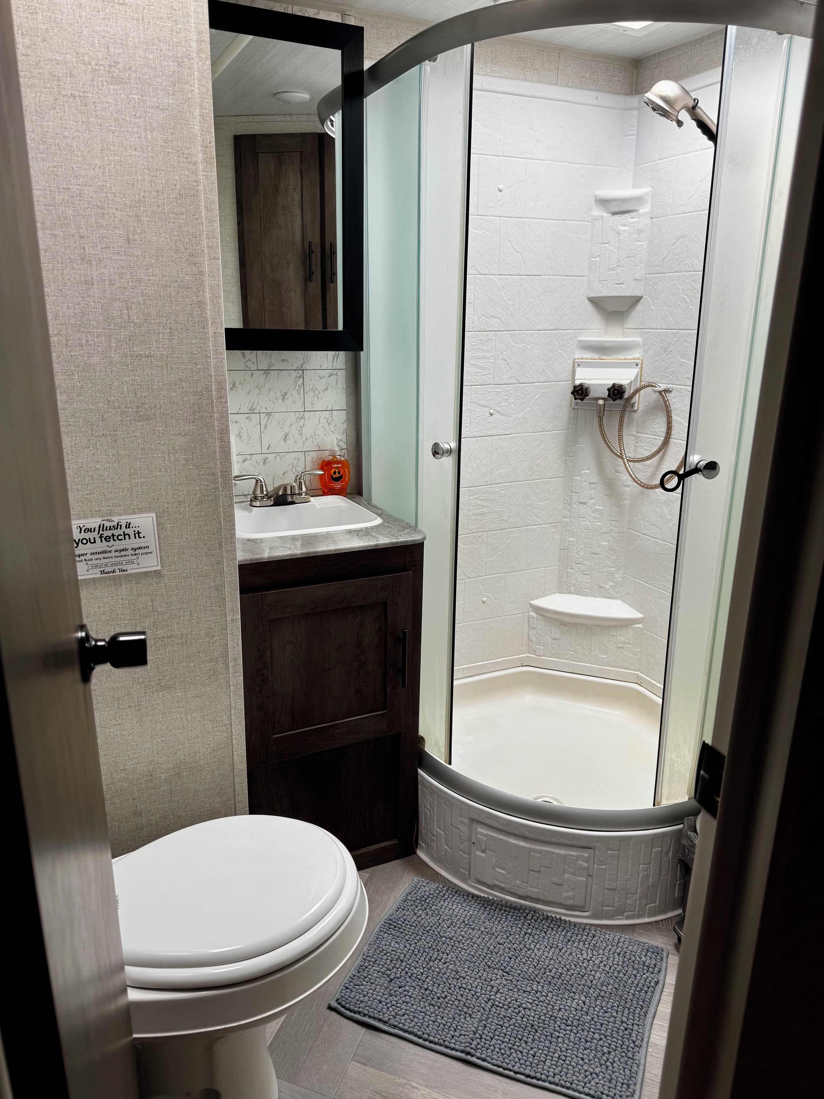 A bathroom with a toilet, sink, shower, and a sign on the wall.