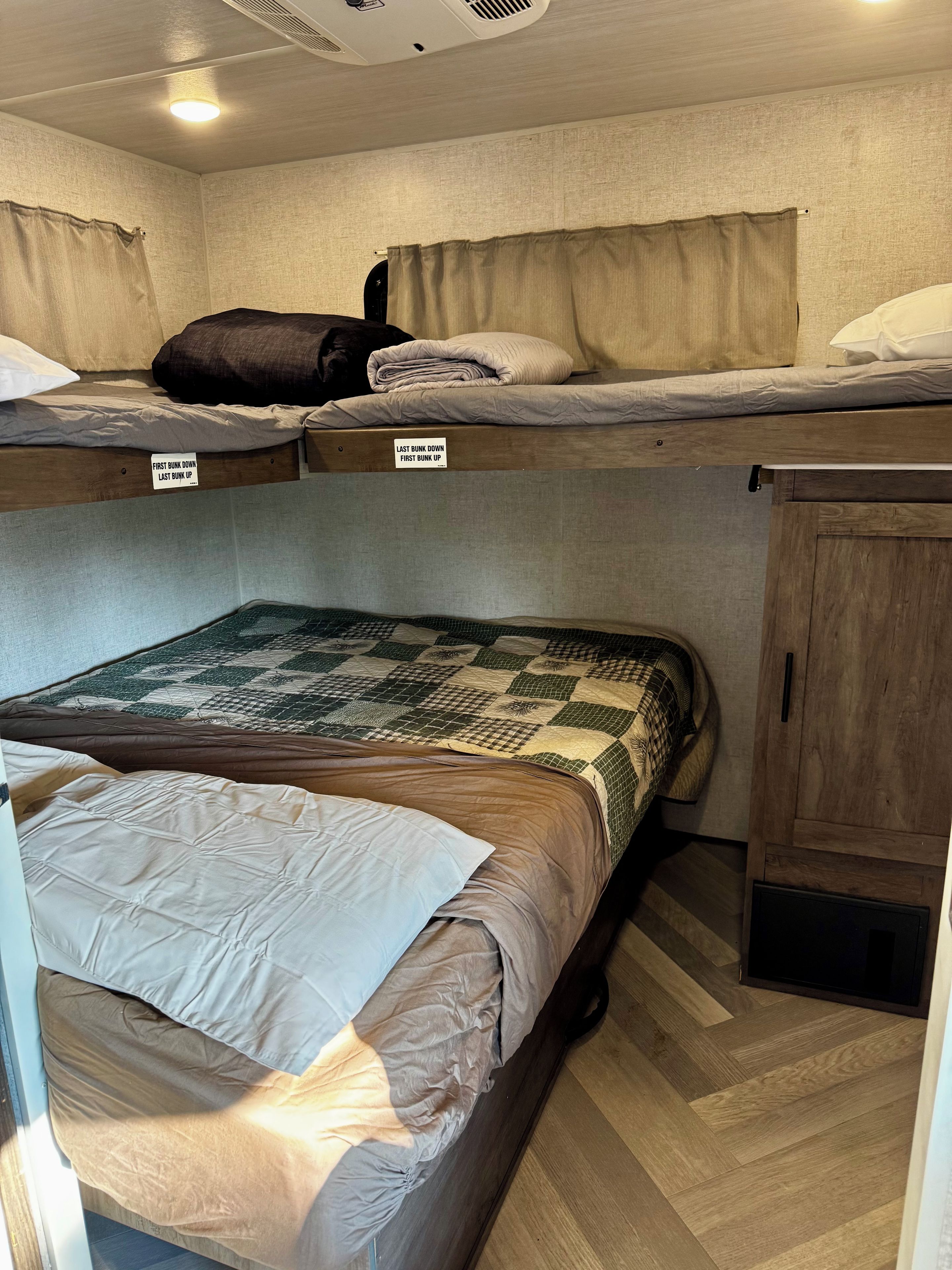 Una cama litera con indicaciones de las posiciones superiores e inferiores, un armario de madera y una colcha estampada en la cama inferior.