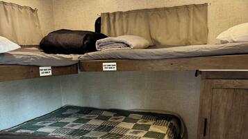 Una cama litera con indicaciones de las posiciones superiores e inferiores, un armario de madera y una colcha estampada en la cama inferior.