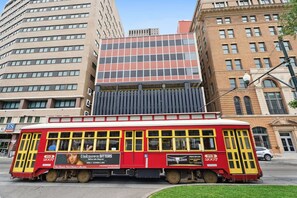 A red trolley with advertisements, parked in front of a building with a large window display. - Luxury 1Bed Room Condo located in Central Business District in french quarters (New Orleans)