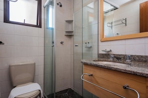 Un baño con inodoro, ducha con puerta de cristal, lavamanos con encimera de granito y tocador de madera.