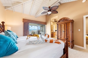 A hotel room with a large bed, a wooden wardrobe, a ceiling fan, and a view of the ocean through a sliding door. - PS 126 - Ocean View • Near Shipwreck Beach (Poipu)