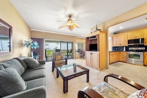 A living room with a sofa, a glass coffee table, and a dining area with chairs. - PS 126 - Ocean View • Near Shipwreck Beach (Poipu)