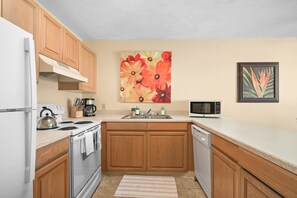 A kitchen with wooden cabinets, a white refrigerator, a stove, a microwave, and a coffee maker. - PK F206 - Ocean View • AC • Pool & Jacuzzi (Kapaa)