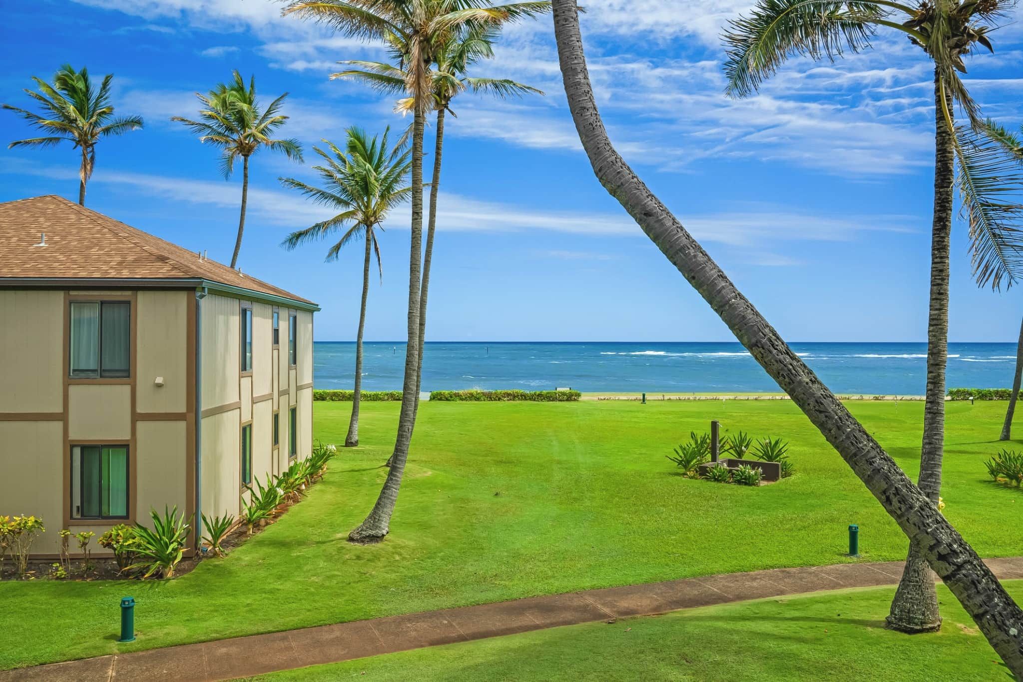 A beachfront property with a well-maintained lawn, palm trees, and a building with a tiled roof.
