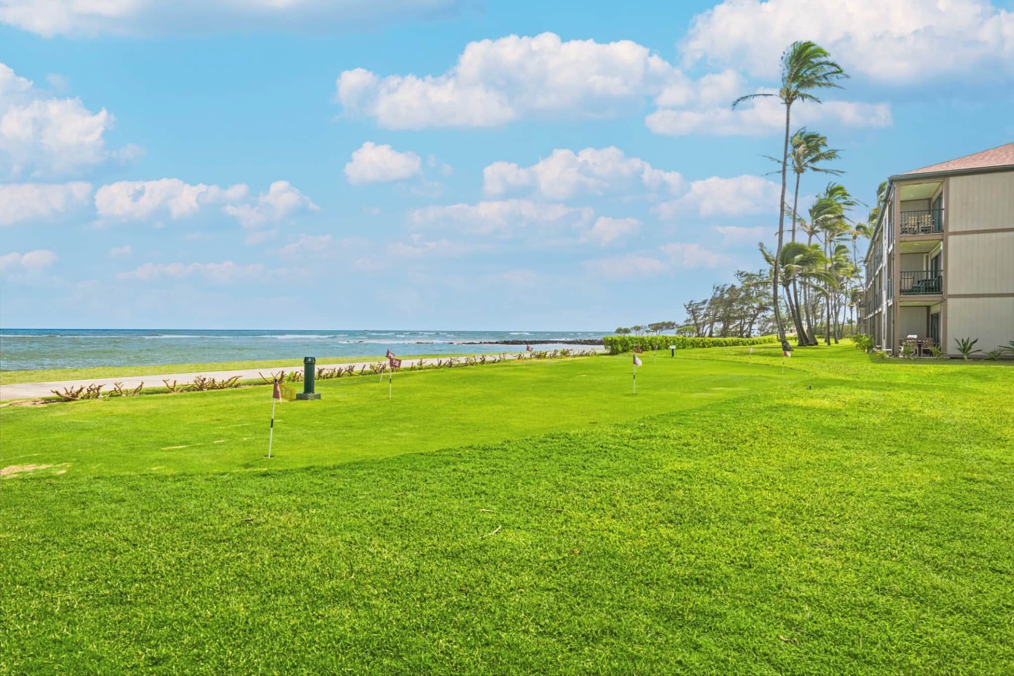 Ein gepflegter Golfplatz mit freiem Blick auf den Ozean und einem Gebäude mit Balkonen.