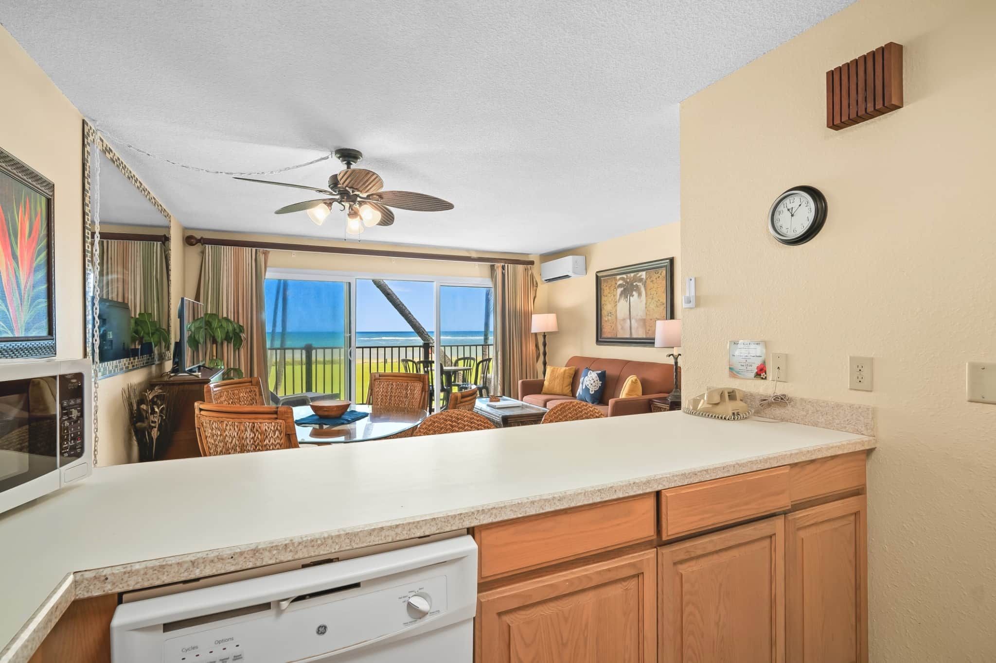 A kitchen with a large island, a dining area with wicker chairs, a ceiling fan, and a view of the ocean.