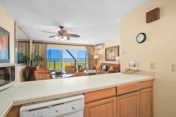 A kitchen with a large island, a dining area with wicker chairs, a ceiling fan, and a view of the ocean.