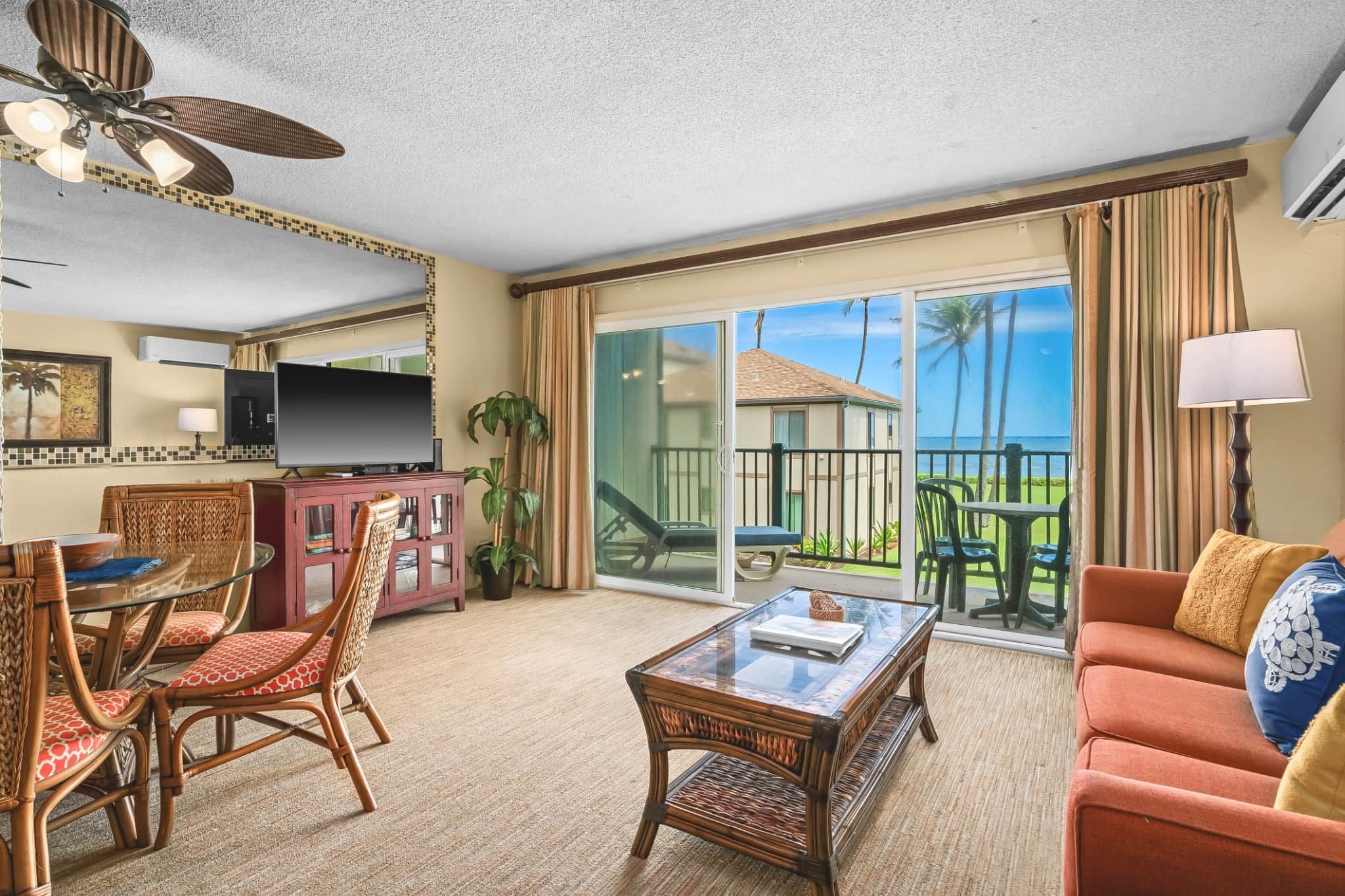 A hotel room with a balcony, a television, a dining area with wicker chairs, and a sofa.