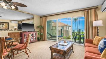 A hotel room with a balcony, a television, a dining area with wicker chairs, and a sofa.