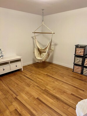Ein Zimmer mit Holzboden, einem weißen Schminktisch mit Schubladen, einem Hängekorbsessel und mehreren gestreiften Aufbewahrungsboxen.