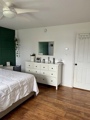Ein Schlafzimmer mit Bett, Kommode, Spiegel und einer Tür.