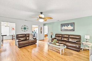 Ein geräumiges Wohnzimmer mit zwei Ledersofas, einem Couchtisch und einem Deckenventilator.