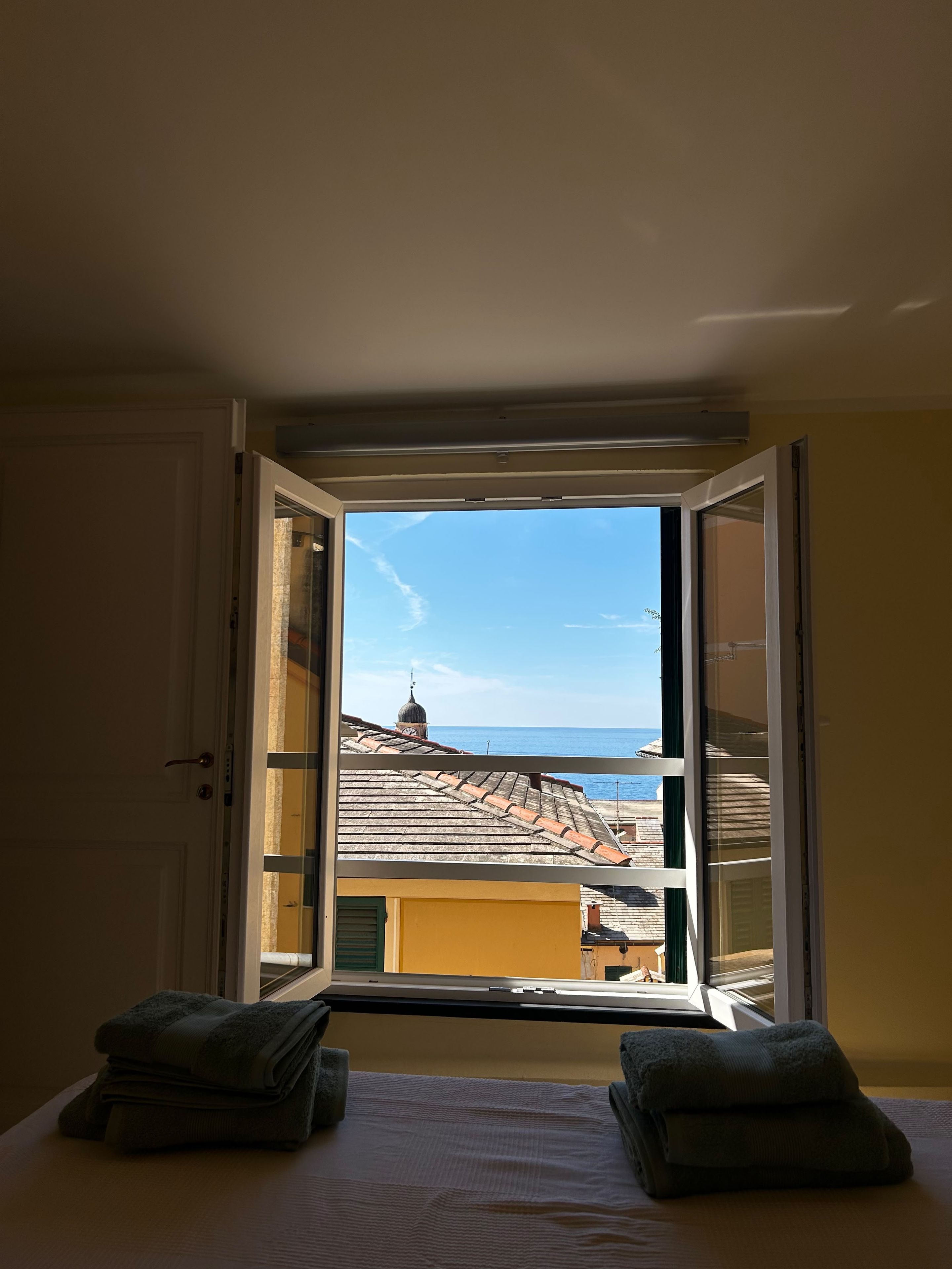 Une chambre avec un lit, une fenêtre et une vue sur les bâtiments et la mer.