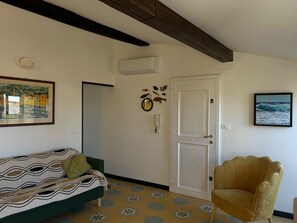Ein Zimmer mit einem Bett, einem Sessel, einer Tür und einer Wand mit einem Gemälde.