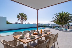 A dining area with a pool view, outdoor seating, and a clear sky. - Vacation Villa 'Ereza Royal Family Hoopoe 113' with Private Pool, Wi-Fi and Air Conditioning (Playa Blanca)