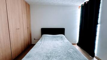 A bedroom with a bed, a wardrobe, and a window with curtains.