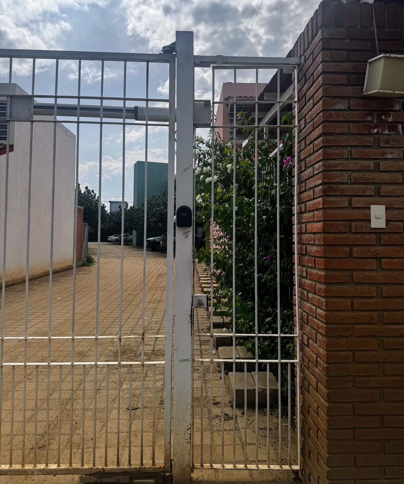 Une entrée fermée par un portail en métal, un mur de briques et une zone pavée où est garé un véhicule.