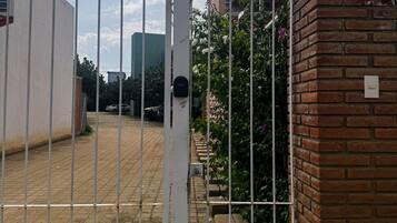 Une entrée fermée par un portail en métal, un mur de briques et une zone pavée où est garé un véhicule.