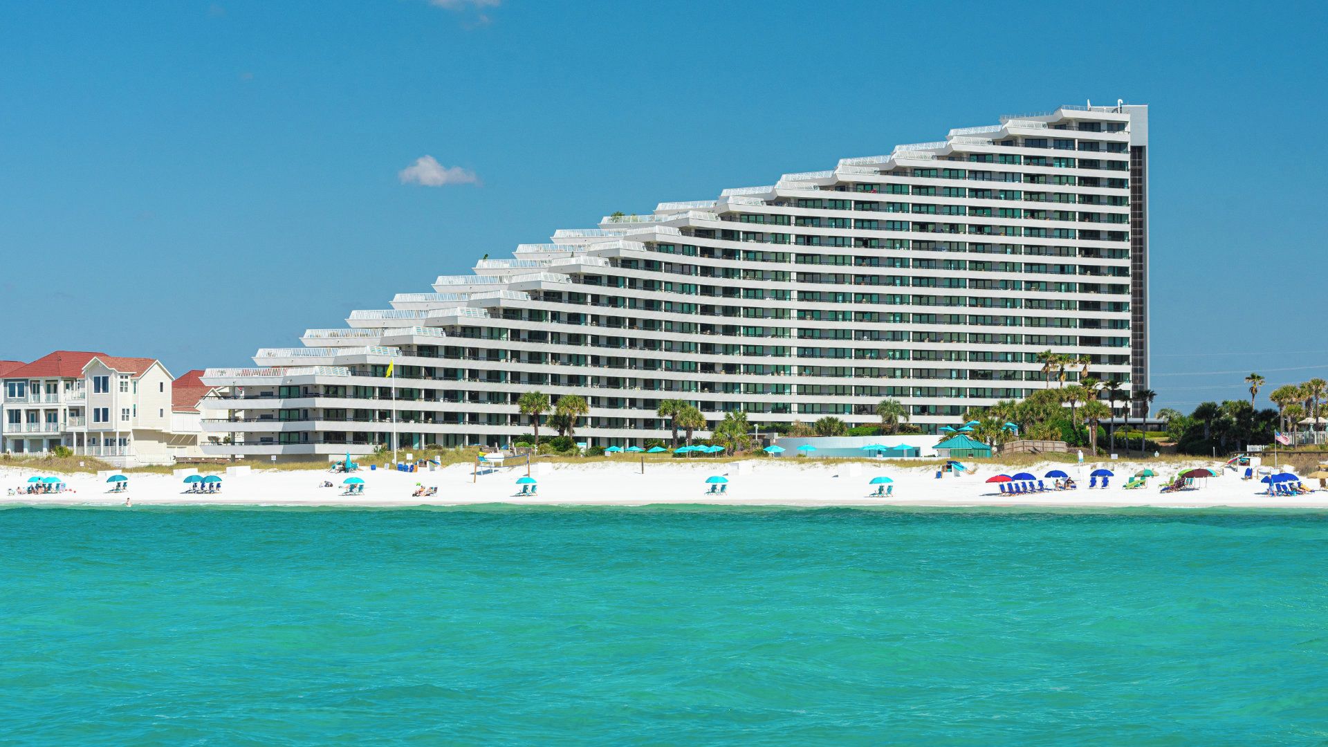 A multi-story hotel with a modern design, located adjacent to a beach with umbrellas and lounge chairs.