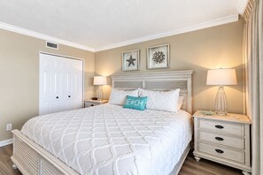A bedroom with a bed, nightstands, a dresser, and a door. - 5-Star Beachfront Condo, Edgewater Resort #1402 (Miramar Beach)