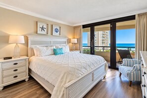 A bedroom with a large bed, a nightstand, a chair, and a view of the ocean. - 5-Star Beachfront Condo, Edgewater Resort #1402 (Miramar Beach)