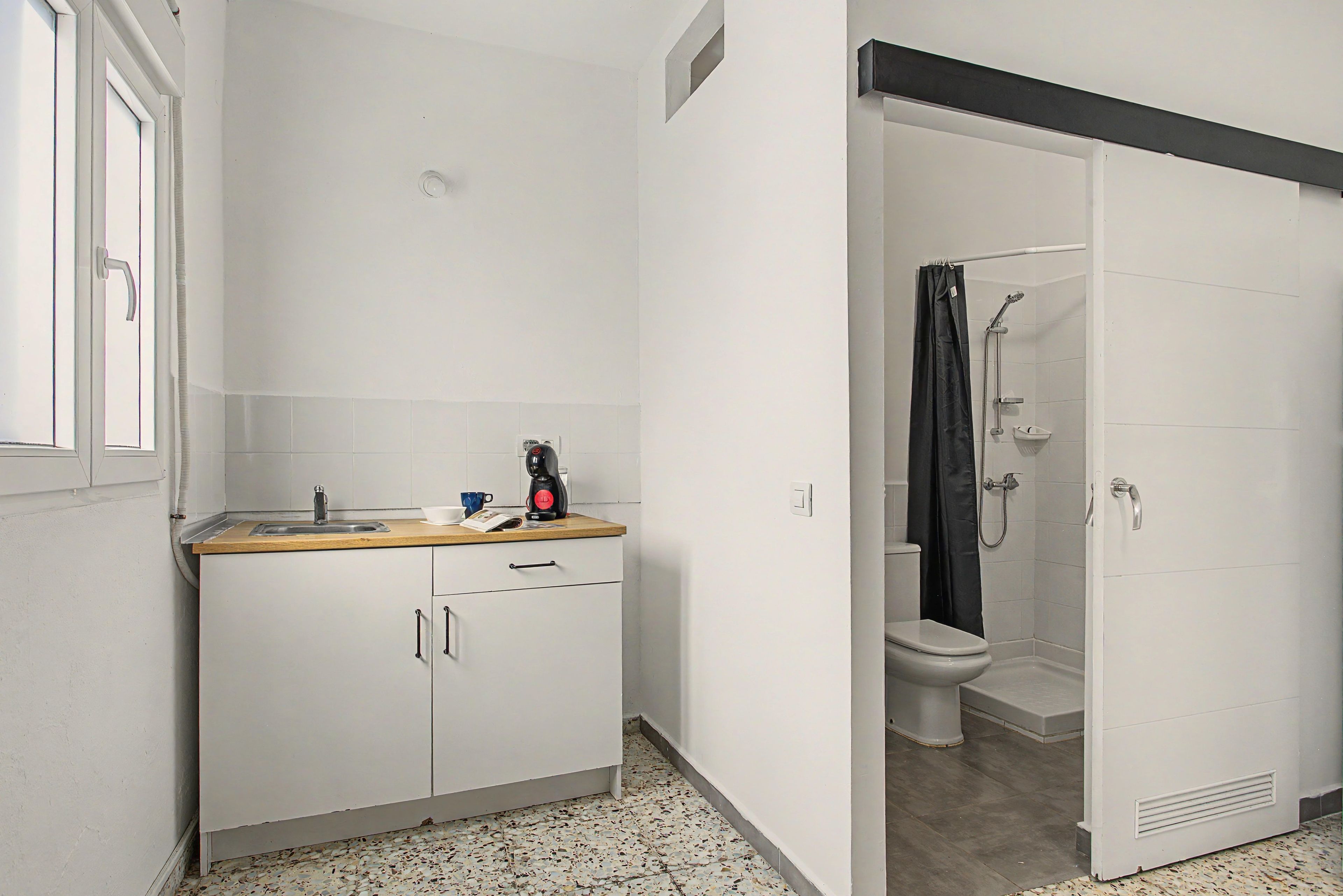 Un baño pequeño con ducha, inodoro y una kitchenette con lavamanos y armarios.