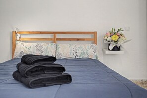 A neatly made bed with a blue bedspread and pillows, a wooden headboard, a bedside lamp, and a wall-mounted flower arrangement. - Vacation Apartment 'A' with Wi-Fi and Air Conditioning (San José de los Llanos)