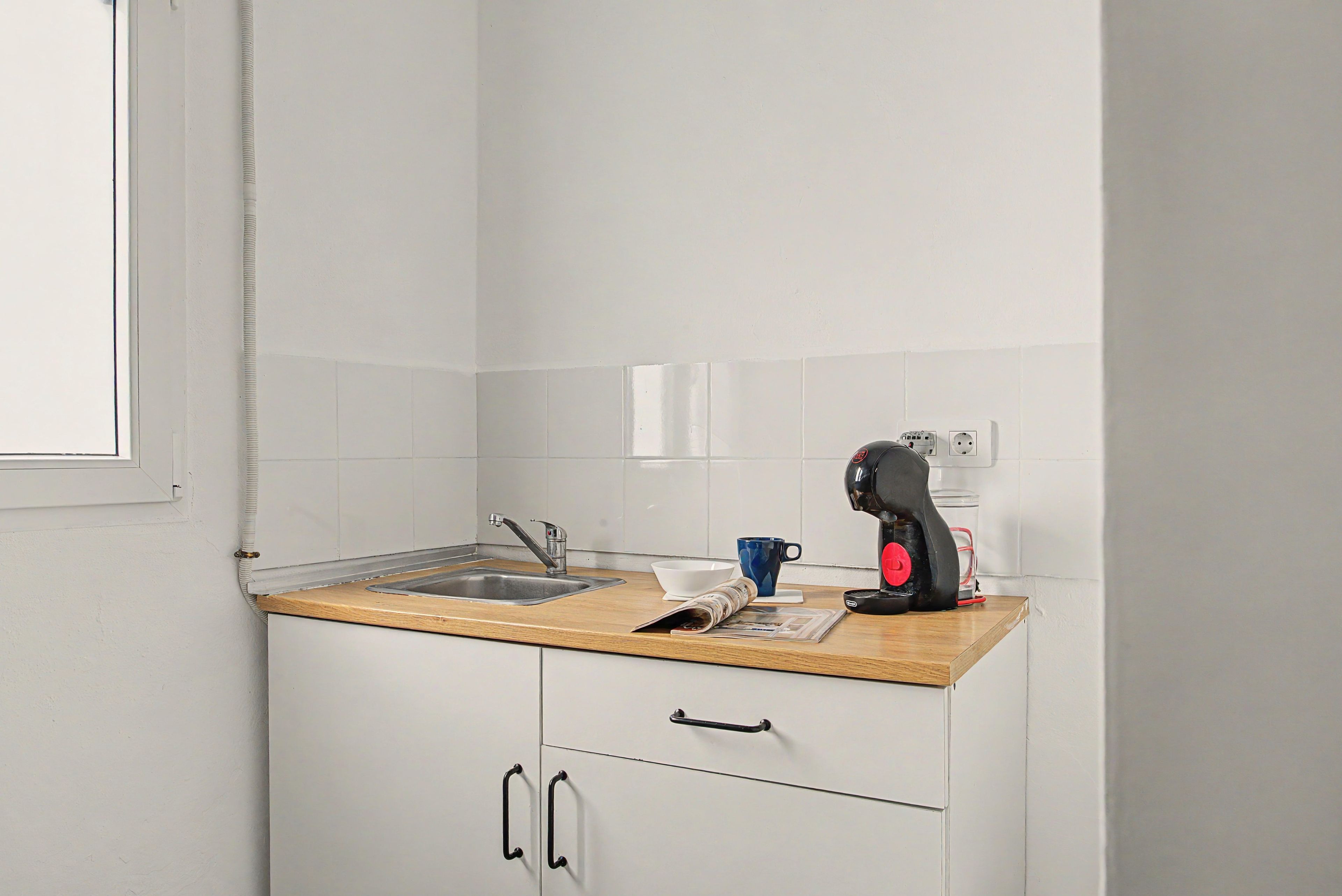 Una kitchenette pequeña con un lavabo, una cafetera, un tazón y una taza sobre la encimera.