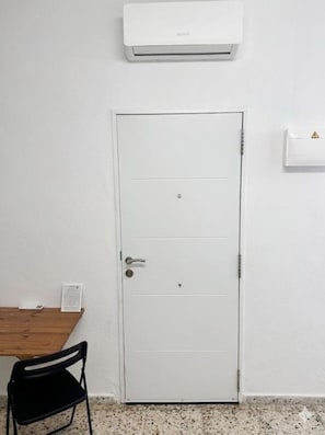A white door with a handle, a small table with a chair, and an air conditioning unit mounted on the wall. - Vacation Apartment 'A' with Wi-Fi and Air Conditioning (San José de los Llanos)